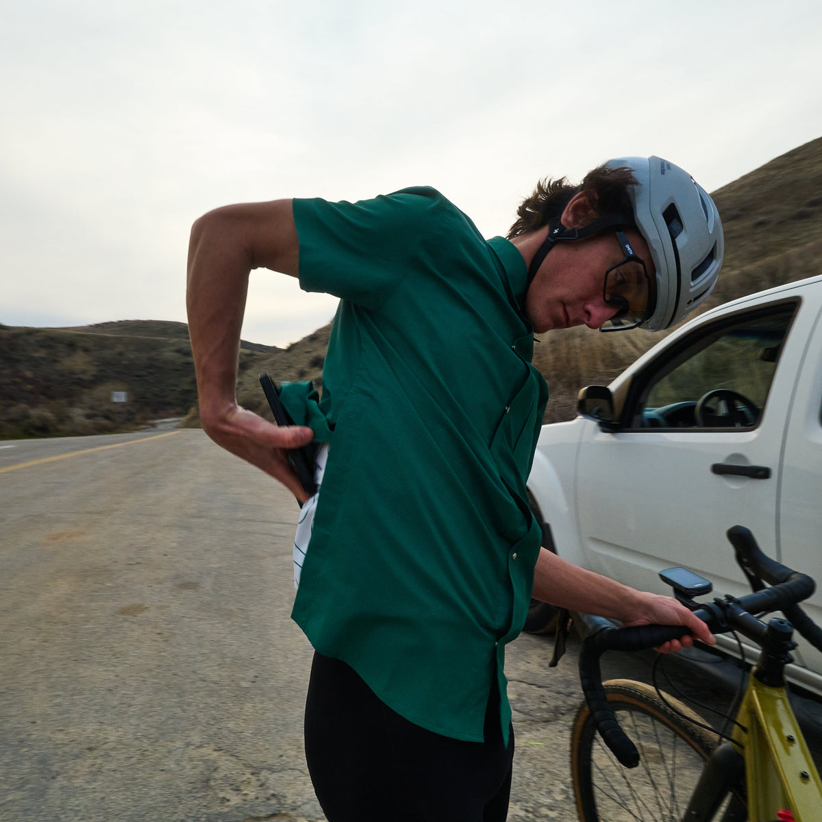 Person with a bicycle on the side of a road with a white car and mountains in the background